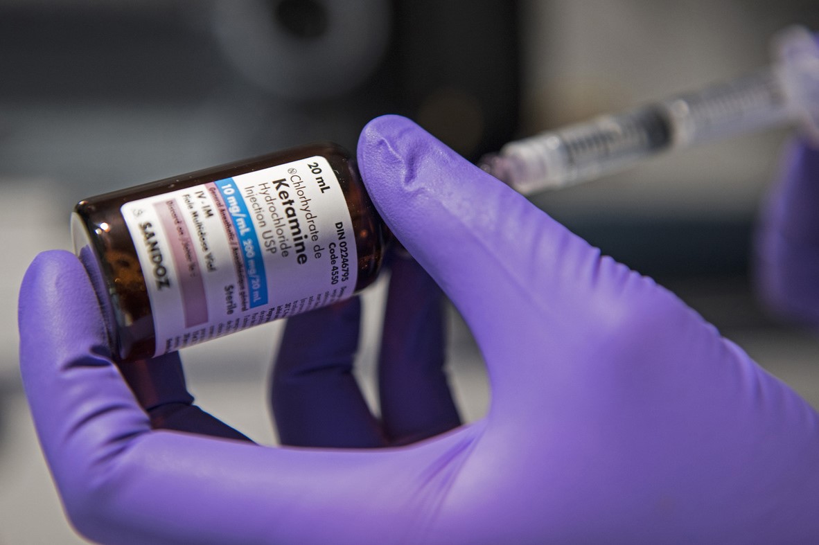 Gloved hand holding ketamine vial and syringe.